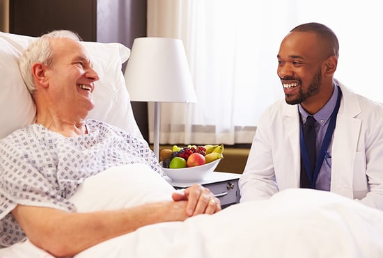 Image of an older man laying in a hospital bed talking to his doctor about regular yearly screenings for bladder cancer