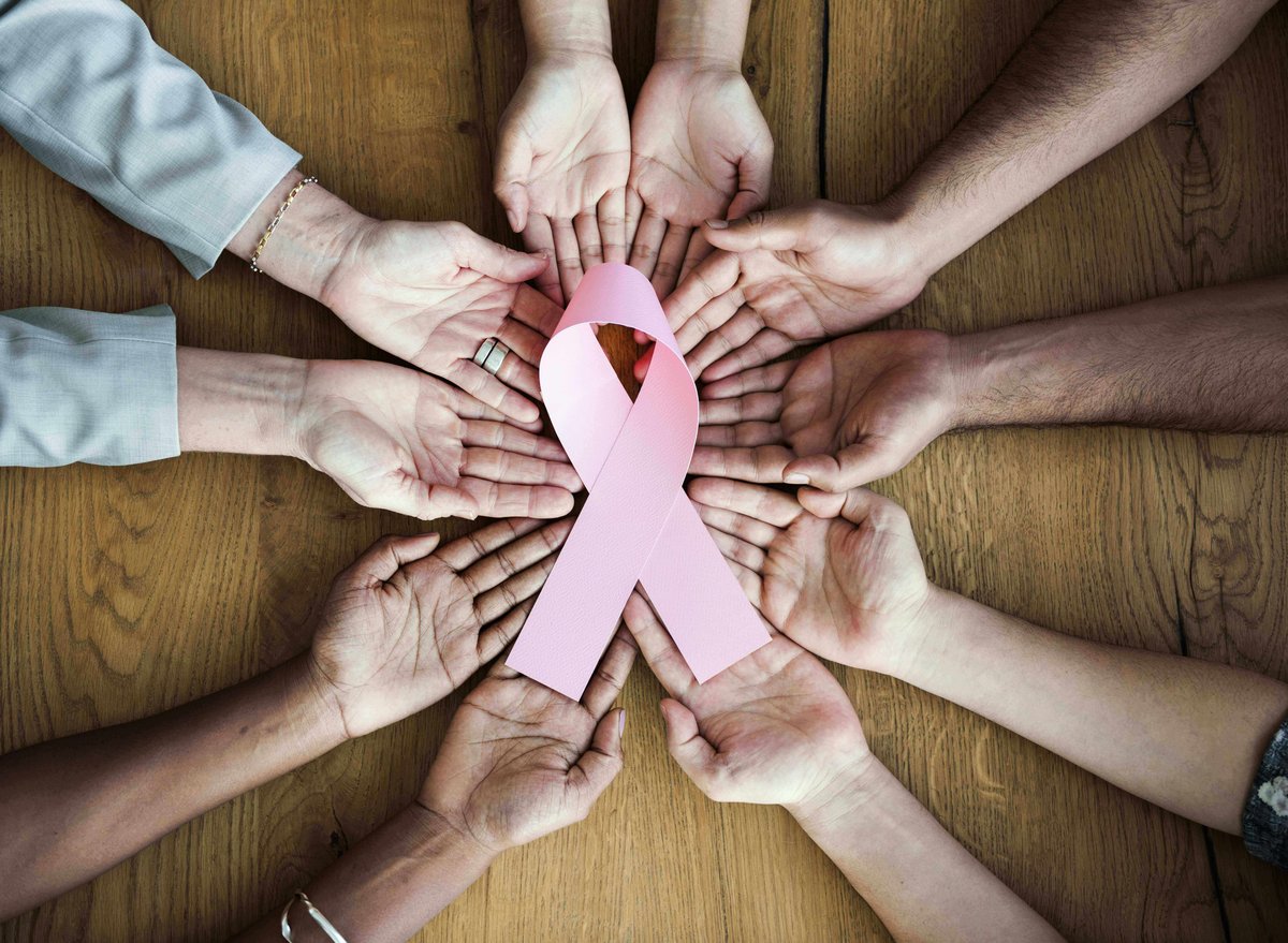 Group of hands holding a pink ribbon representing break caner awareness.