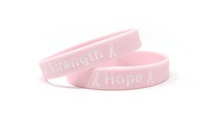 Image of two light pink silicone wristbands with breast cancer awareness messages