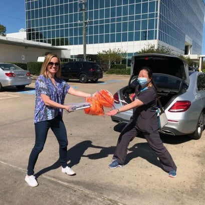 Woman handing PPE donations to healthcare worker in the parking lot of a hospital.