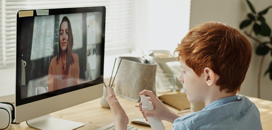 A boy talking to his mom on a computer screen while using hand sanitizer